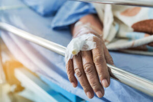 an elderly person's hand with an IV port rests on a bed rail